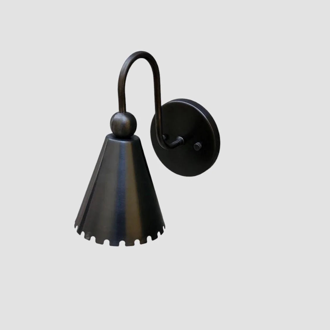 Black wall-mounted lamp with cone-shaped shade on a light gray background
