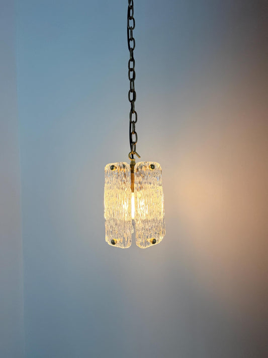 A hanging pendant light with two textured clear glass shades suspended by a dark metal chain, glowing with a warm yellow light against a soft blue wall.