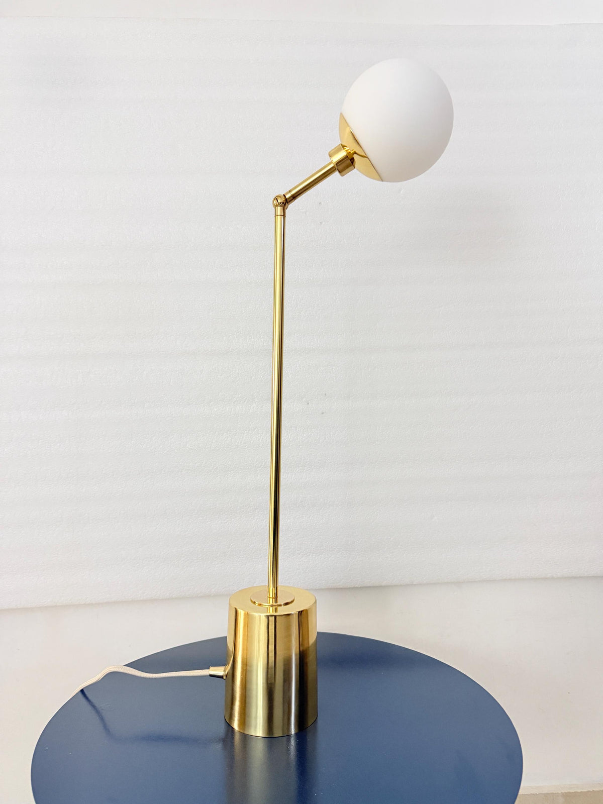 A Compact Globe Table Lamp Shown with A Warm Brass Finish, Rounded Opal Glass Shade, Articulating Arm, and Cylindrical Base. the Combination of Metal and Softly Diffusing White Glass Gives the Handmade Fixture a Clean Mid Century Inspired Appearance, Frost Lights.