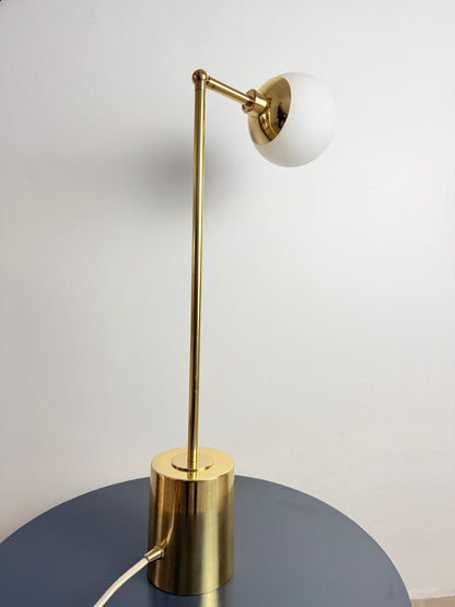 A Clean Contemporary Table Lamp Made with Brass Construction and An Opal White Glass Globe, Featuring an Adjustable Arm Above a Compact Cylindrical Base. the Fixture Has a Restrained Silhouette that Blends Naturally with Modern and Mid Century Interiors, Frost Lights.