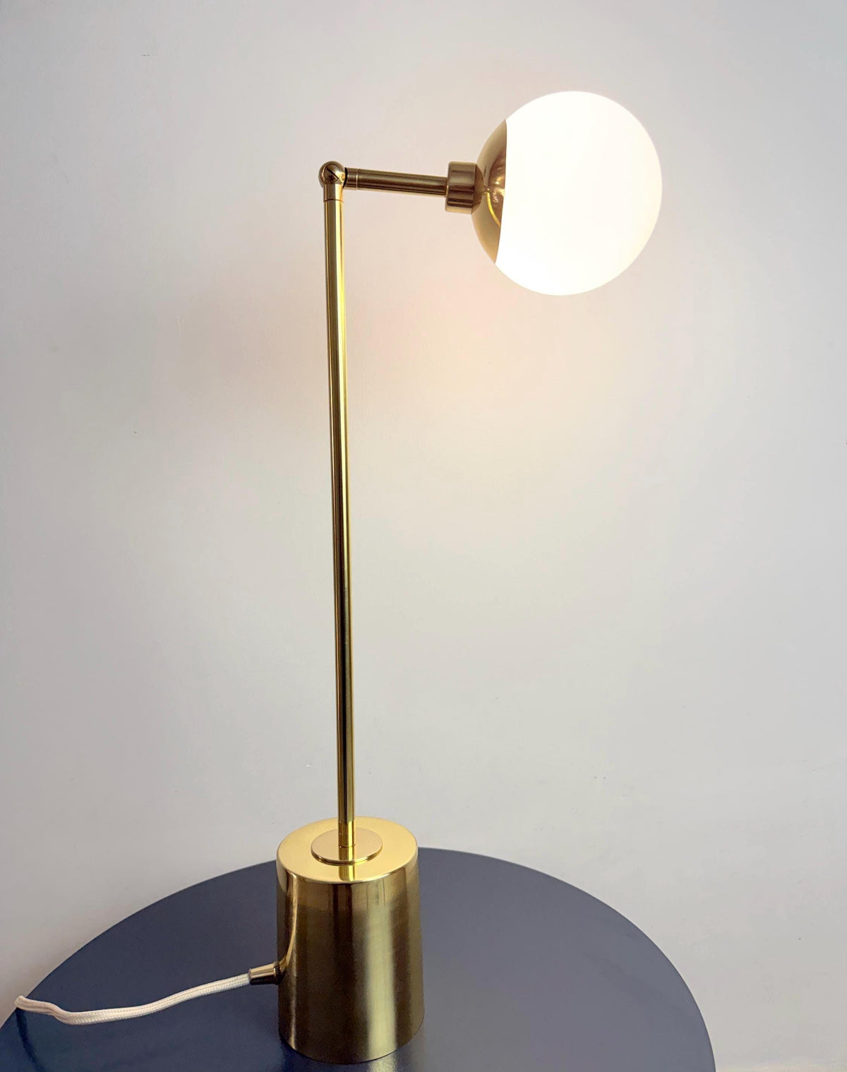 A Handmade Brass Table Lamp with A Slim Vertical Stem, Adjustable Articulating Arm, and Softly Rounded Opal White Globe Shade, Standing on A Compact Cylindrical Base. the Simple Silhouette Suits Bedside Tables, Desks, and Minimalist Interiors, Frost Lights.