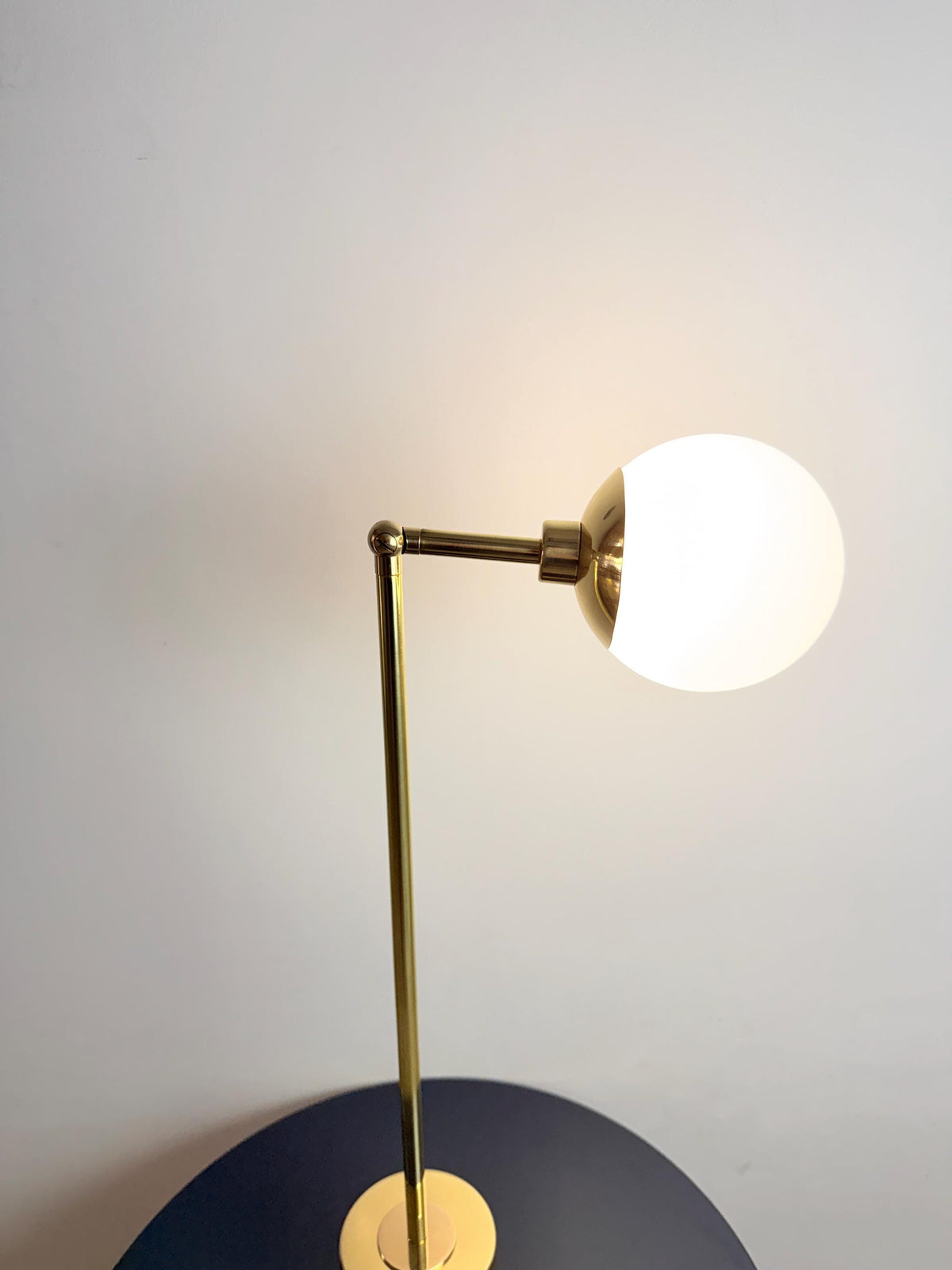 A Sculptural Brass Bedside Lamp with A Smooth Globe Shaped Opal Glass Shade and Adjustable Arm. the Vertical Stem Rises from A Compact Cylindrical Base, Giving This Plug in Table Fixture a Balanced Silhouette with Understated Modern Character, Frost Lights.