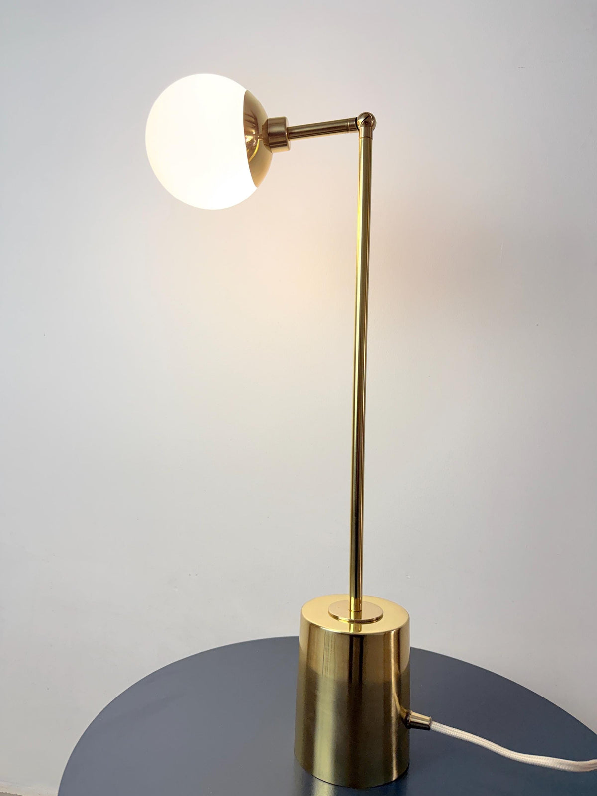 A Refined Brass Desk Lamp Featuring a Rounded Opal Globe Shade, Adjustable Articulating Arm, Slender Vertical Stem, and Stable Cylindrical Base. Its Simple Geometry Brings Together Functional Lighting and A Restrained Mid Century Modern Inspired Aesthetic, Frost Lights.