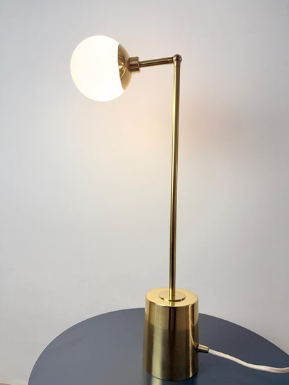 A Refined Brass Desk Lamp Featuring a Rounded Opal Globe Shade, Adjustable Articulating Arm, Slender Vertical Stem, and Stable Cylindrical Base. Its Simple Geometry Brings Together Functional Lighting and A Restrained Mid Century Modern Inspired Aesthetic, Frost Lights.