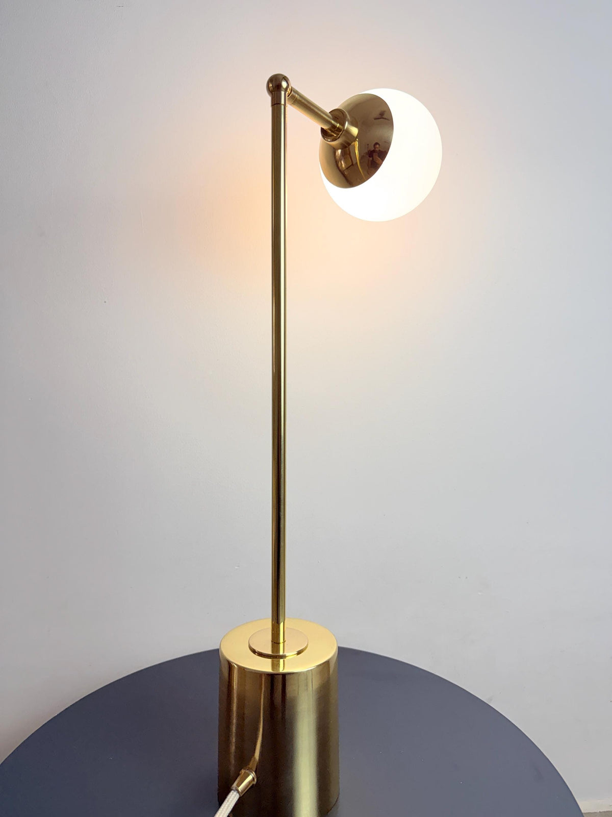 Seen from An Angled View, This Handmade Table Lamp Highlights the Relationship Between Its Adjustable Brass Arm and Matte Opal White Globe. the Slim Stem and Compact Cylindrical Base Keep the Fixture Visually Clean and Suitable for Contemporary Interiors, Frost Lights.