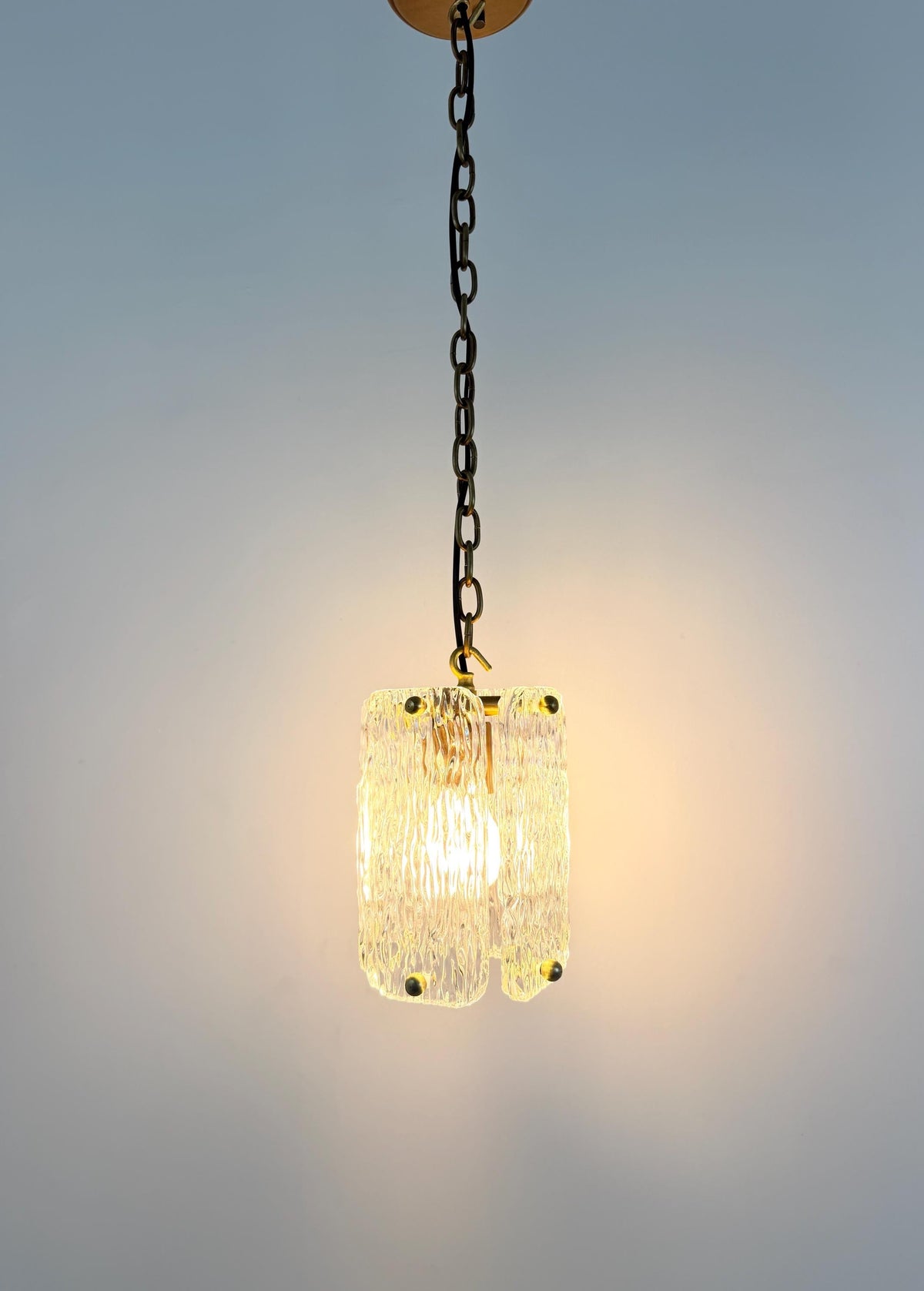 Textured glass lantern-style pendant light with brass details for home interiors.