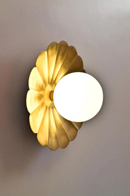 Vintage brass chandelier with a petal-shaped backplate and round white glass bulb, mounted on a wall.